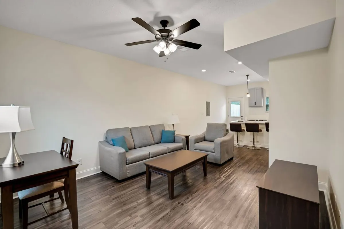 This image features a spacious open-concept living and dining area, with a cozy sofa set arranged around a coffee table and a dining table in the background. Warm light from a stylish overhead fixture creates a welcoming ambiance, inviting guests to relax or gather for shared meals and conversation.