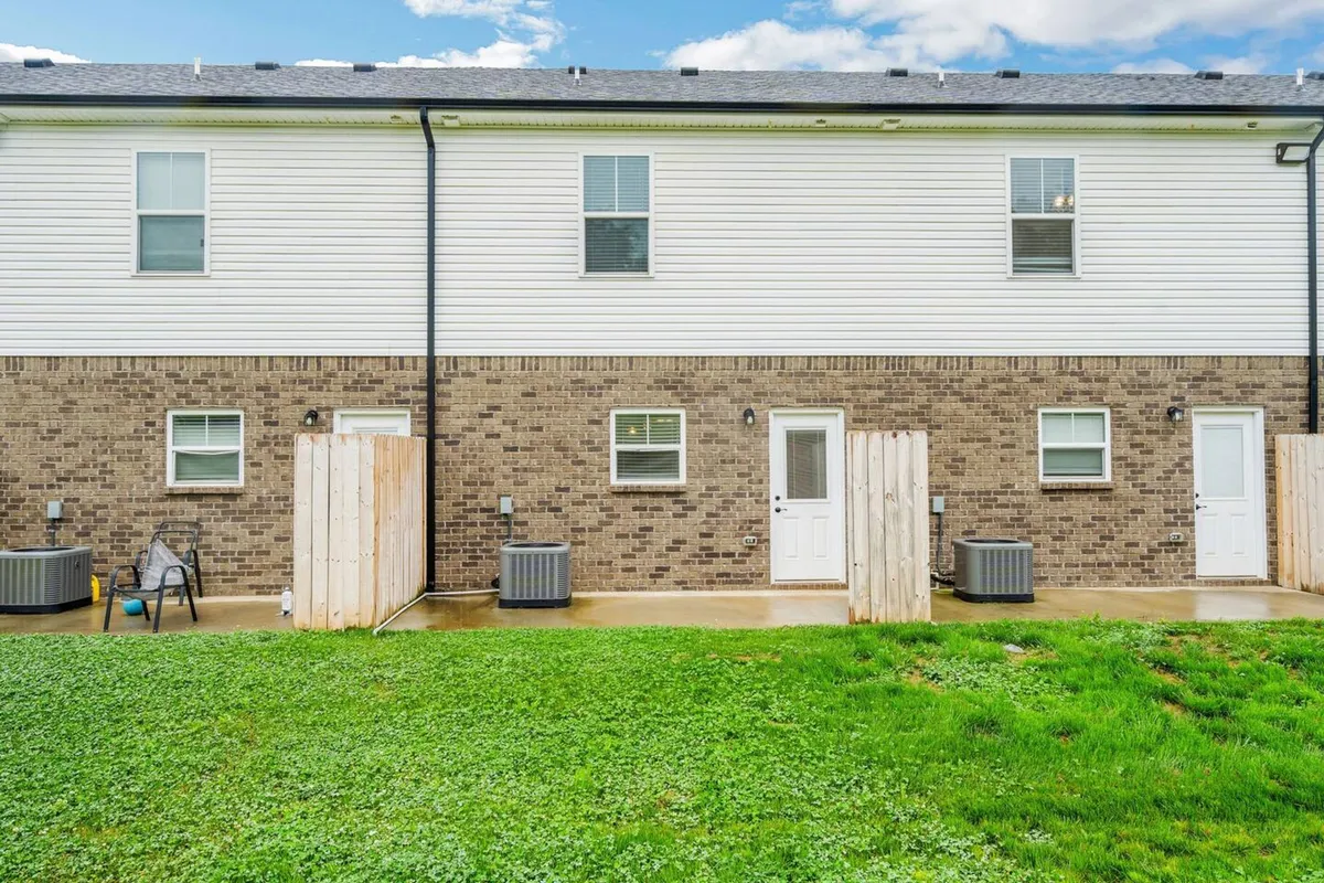 An exterior setting featuring a comfortable lawn area with brick and white siding in the background, bordered by a fence. The scene suggests opportunities for outdoor relaxation or informal gatherings after a long workday.
