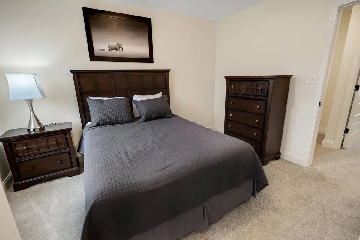 This bedroom image highlights a serene and inviting space with a comfortable bed, a nightstand, a dresser, and wall art. Morning light streams in, enhancing the sense of peace and making it ideal for restful sleep or leisurely mornings.