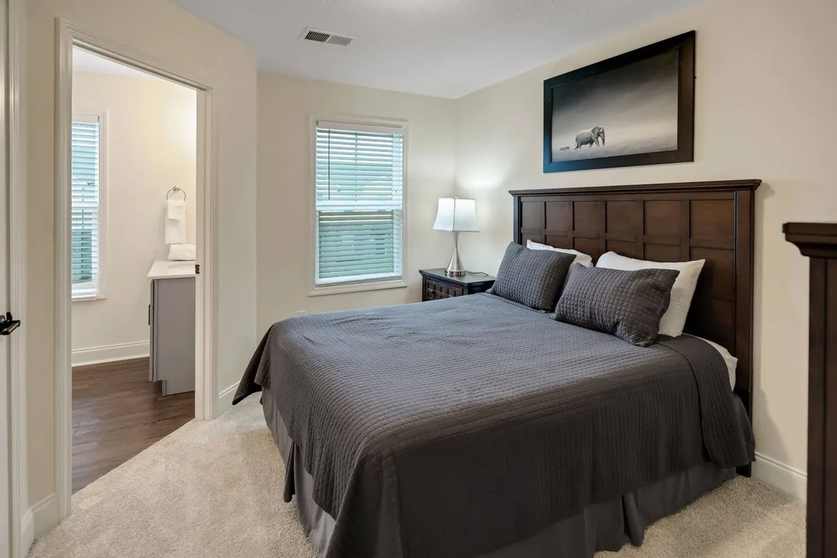 This image shows a tranquil bedroom featuring a neatly made bed, a nightstand with a lamp, and artwork on the wall. The space is inviting, designed for relaxation, reading, or simply unwinding after a day out. Soft lighting and warm tones create a sense of calm and comfort.
