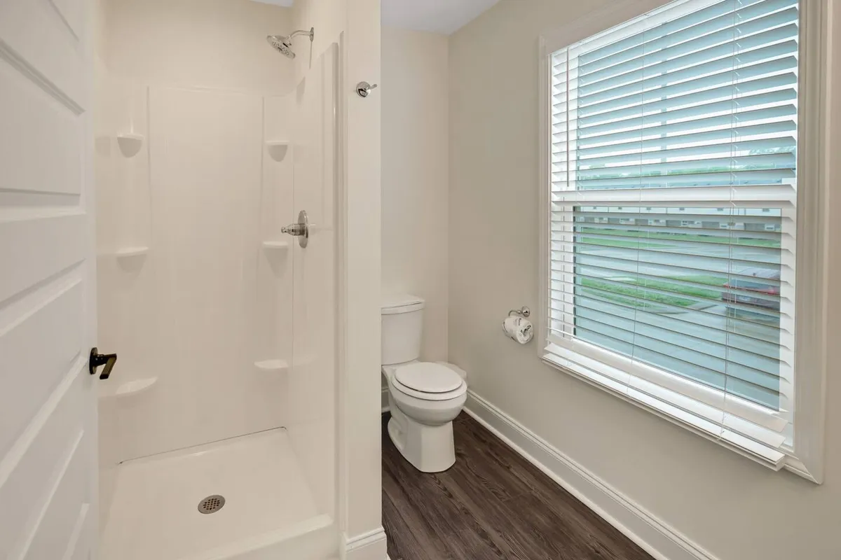 This image showcases a clean and modern bathroom with a spacious shower area, a window providing natural light, and a practical layout. The setting exudes a sense of privacy and refreshment, ideal for personal hygiene routines or unwinding after a demanding day.
