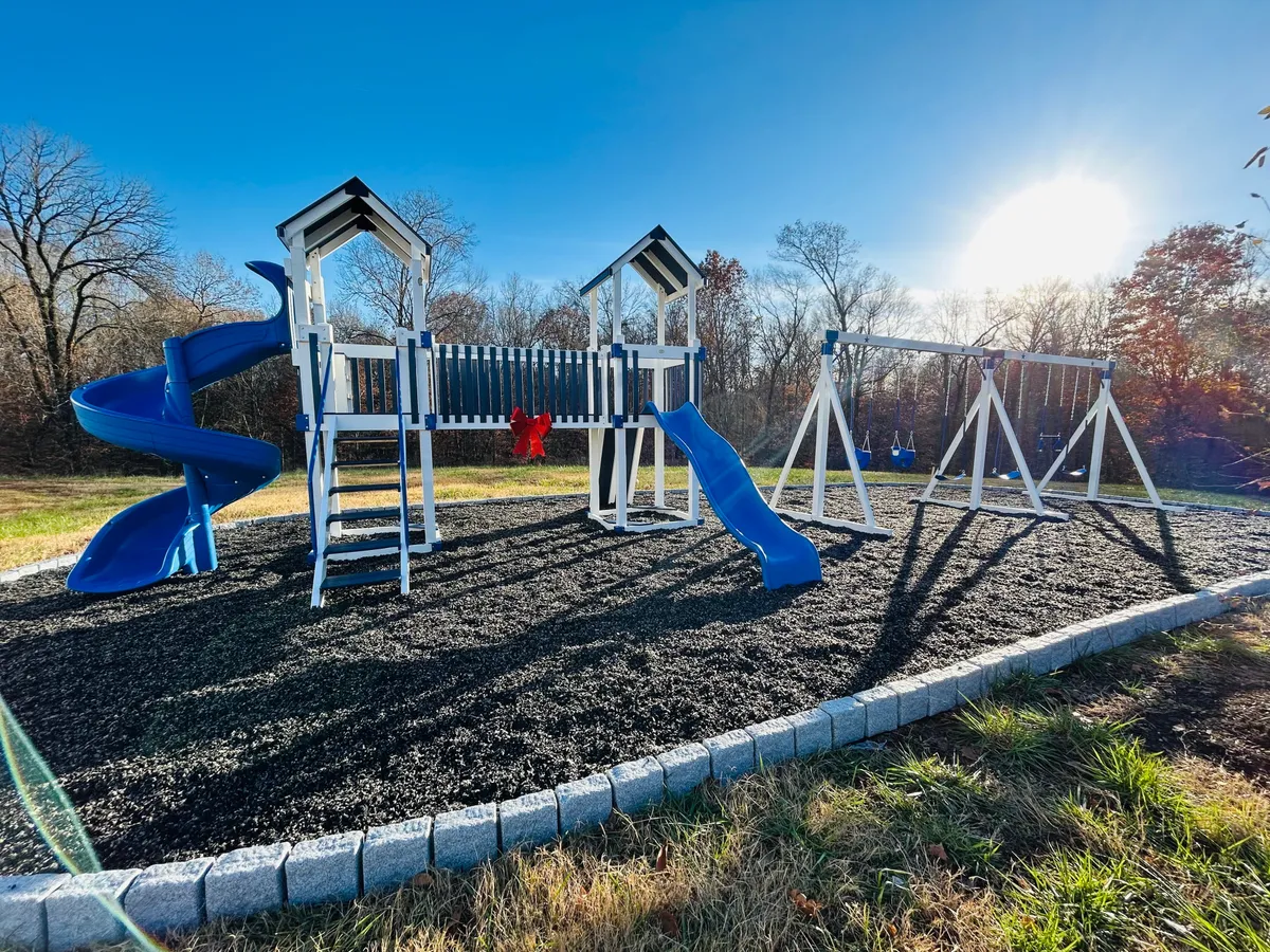 An outdoor playground with a slide and swings, set in a park-like area with space for children to play and families to gather. The scene feels lively and inviting, showcasing a safe, joyful place for kids to enjoy outdoor activities.