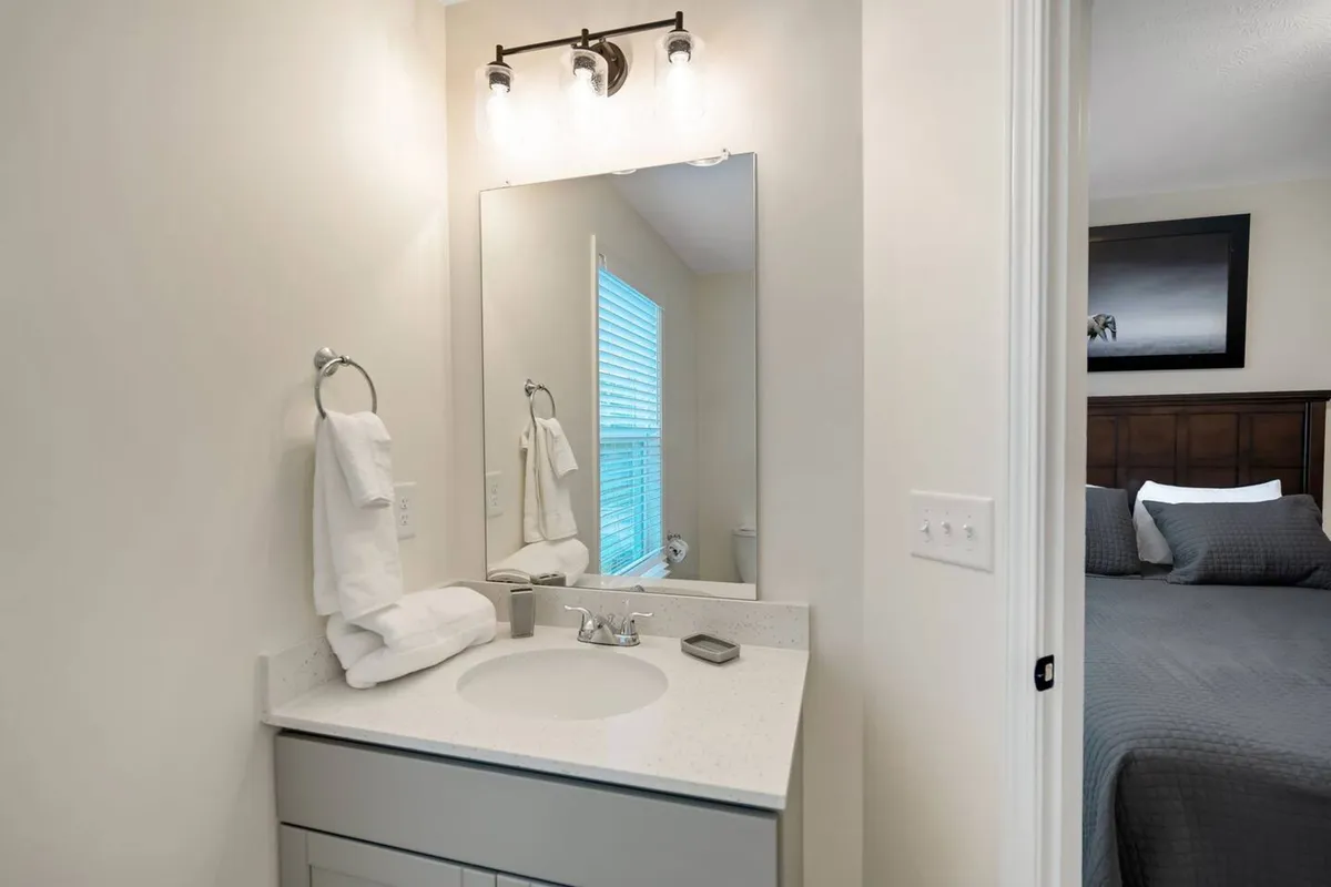 This image features a serene bathroom scene with a mirror, sink, towels, and a window framing the view outside. The soft light and tranquil atmosphere highlight the space’s suitability for both morning routines and moments of calm after a long day.