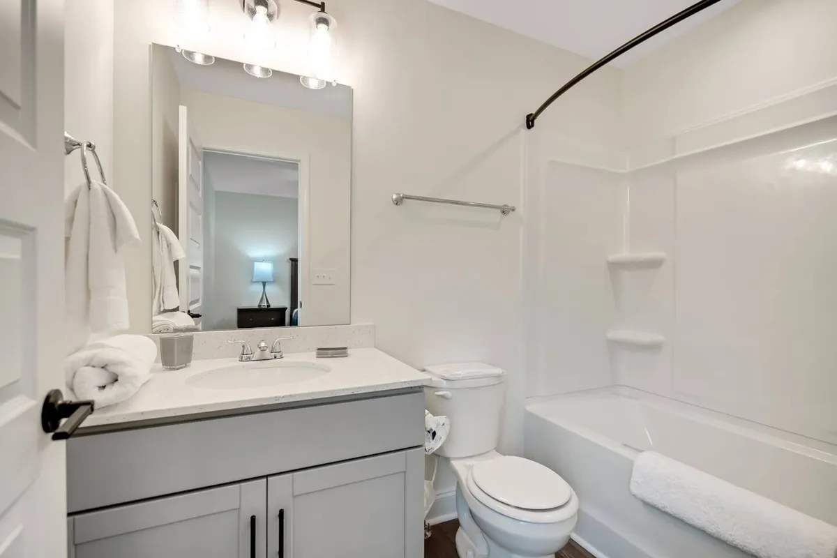 A modern vanity with a sink, a large mirror, and a glimpse of the shower area in a calm, inviting bathroom. The overall atmosphere is one of cleanliness and self-care, with towels and thoughtful details adding to the spa-like ambiance.