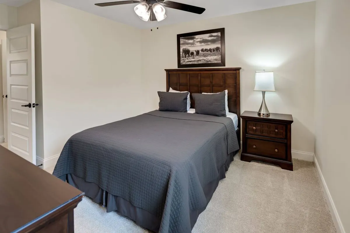 This image features a bed with a dark quilt, complemented by a wooden headboard and a nightstand with a lamp. Framed artwork hangs above the bed, and the overall scene exudes a sense of comfort and tranquility, emphasizing a peaceful environment for rest and relaxation.