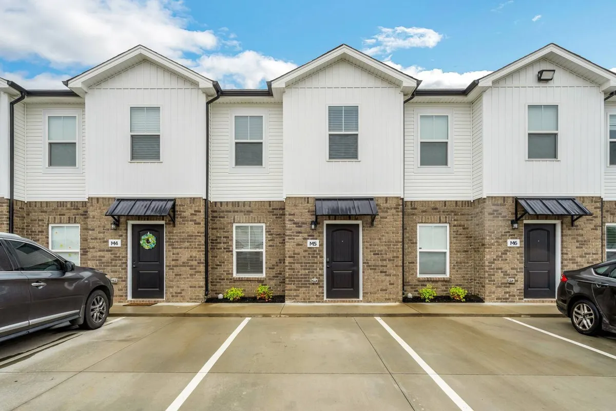A welcoming exterior view featuring the front doors of the residence, visible car parking, and well-maintained landscaping. The scene conveys a sense of arrival, community, and outdoor relaxation possibilities.
